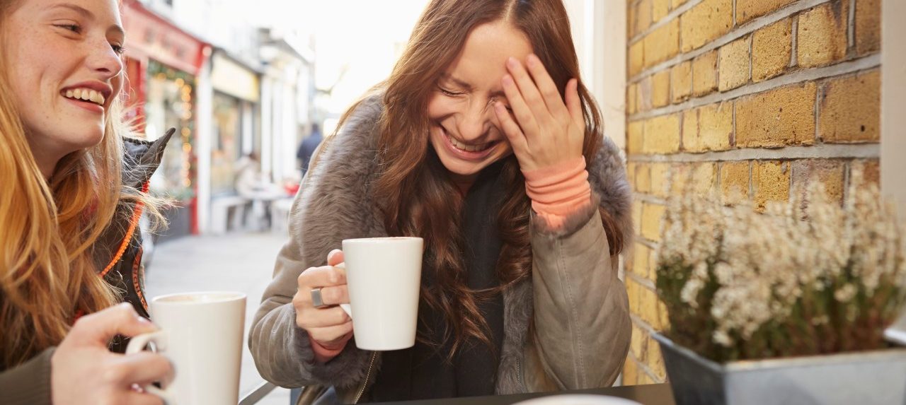 Two female friends sitting in sidewalk cafe laughing --- Image by © Emma Tunbridge/Corbis