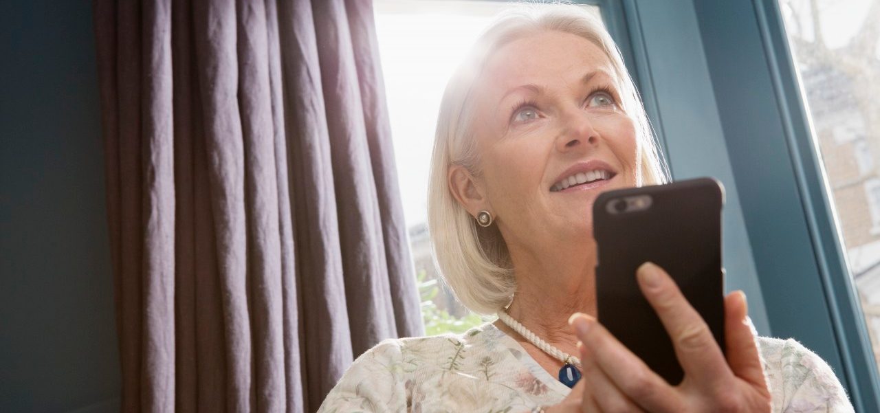 Woman sitting on sofa using smartphone --- Image by © Corbis