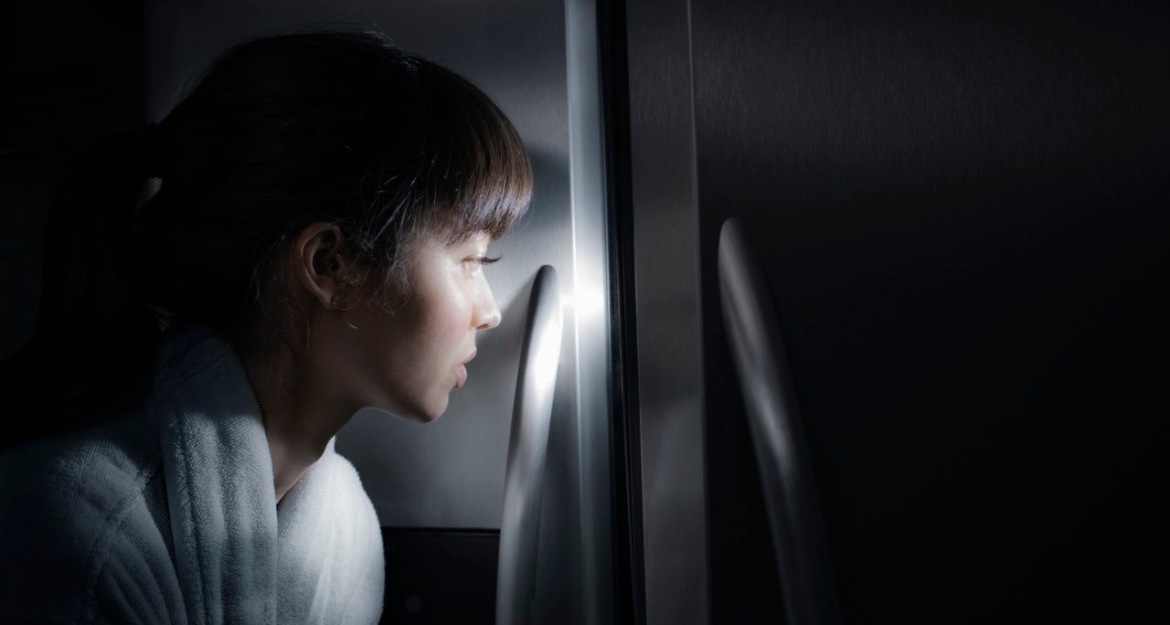 Mixed race woman peering into refrigerator at night --- Image by © Jill Giardino/Blend Images/Corbis