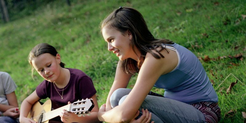 Three Girls Sitting with Guitar in Meadow --- Image by © Mika/Corbis