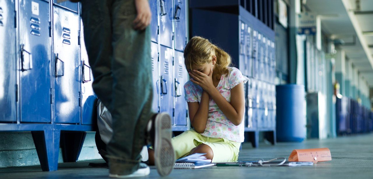 Female junior high student sitting on floor holding head in hands, boy standing smugly nearby --- Image by © Frederic Cirou/PhotoAlto/Corbis