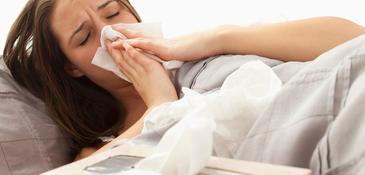 Young woman lying in bed blowing nose --- Image by © Mike Kemp/Tetra Images/Corbis