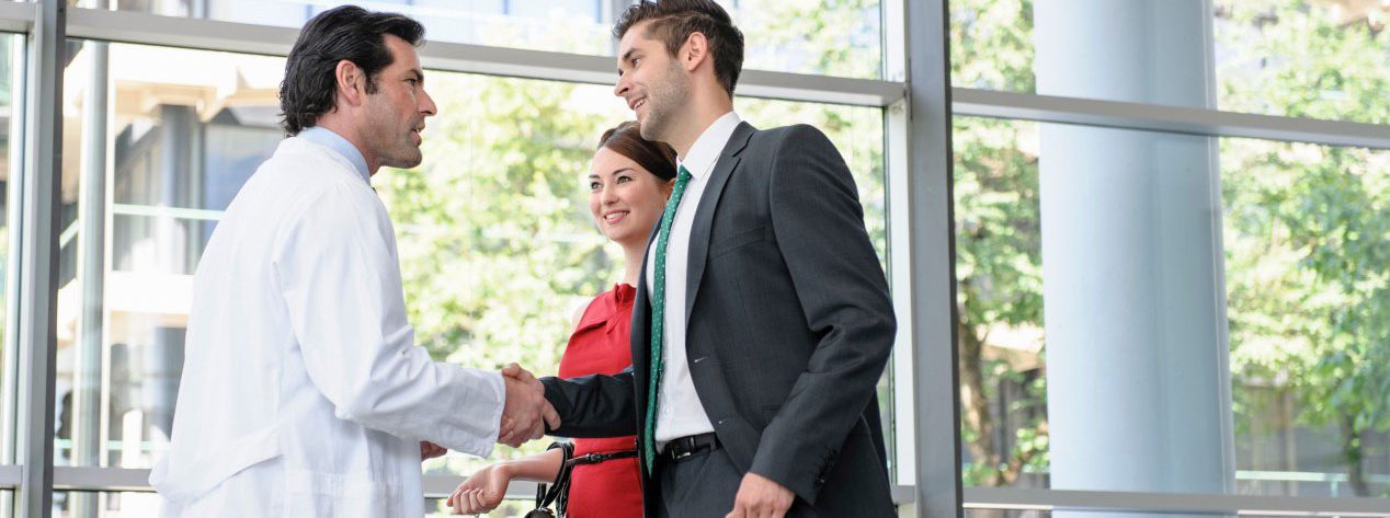 Mature doctor shaking hands with young couple in hospital lobby --- Image by Â© suedhang/cultura/Corbis