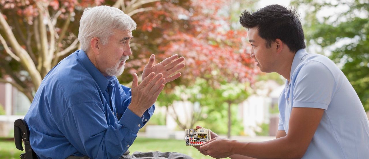 Massachusetts, USA --- Engineer with muscular dystrophy and diabetes in his wheelchair talking with design engineer about microchips on circuit board --- Image by © Mark Hunt/Huntstock/Corbis