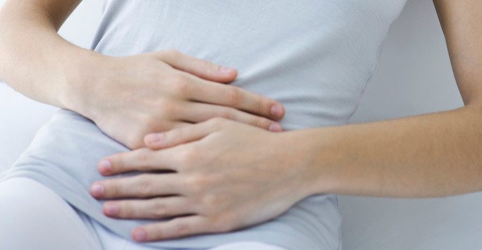 Woman Reclining, Holding Stomach --- Image by © Alix Minde/PhotoAlto/Corbis