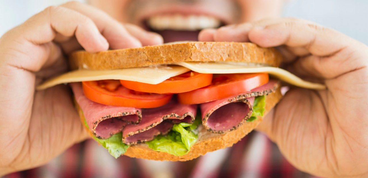 Mixed race man eating sandwich --- Image by © JGI/Tom Grill/Blend Images/Corbis