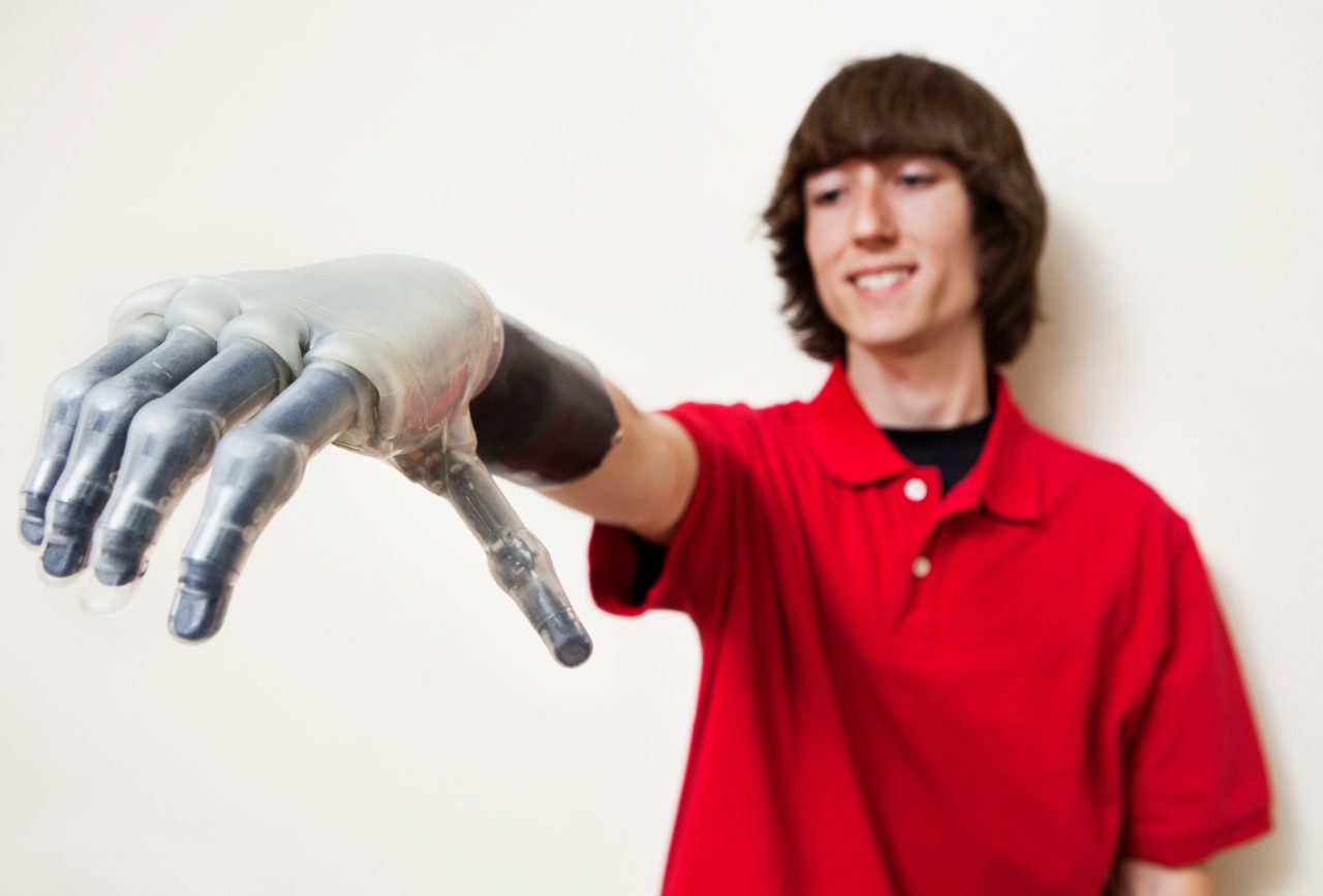 Young man looking at his prosthetic hand over gray background --- Image by © Barry Austin/Moodboard/Corbis