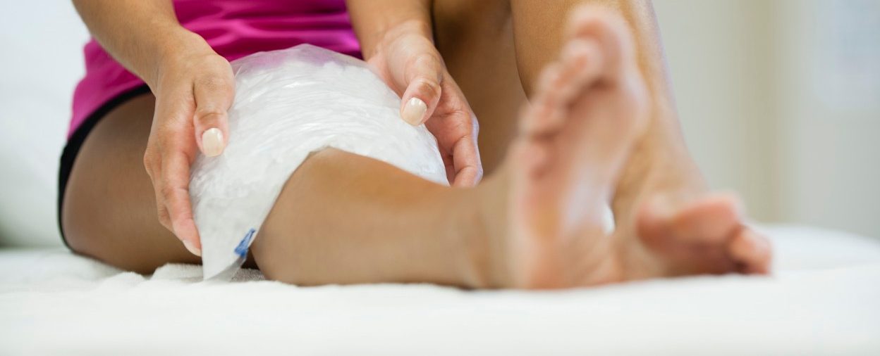 Woman sitting with ice pack on knee --- Image by © Odilon Dimier/PhotoAlto/Corbis