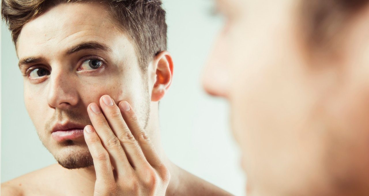 Close-up of young man looking at reflection in bathroom mirror, studio shot --- Image by © Radius Images/Corbis