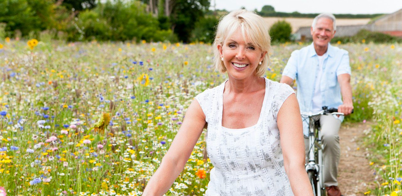 Smiling senior couple riding bicycles on path through field of wildflowers --- Image by © Juice Images/Corbis