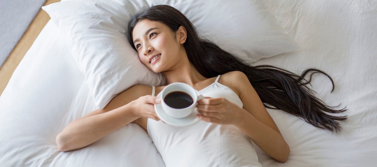 17 Oct 2014 --- Young woman lying on bed with a cup of coffee --- Image by © Lane Oatey/Blue Jean Images/Corbis