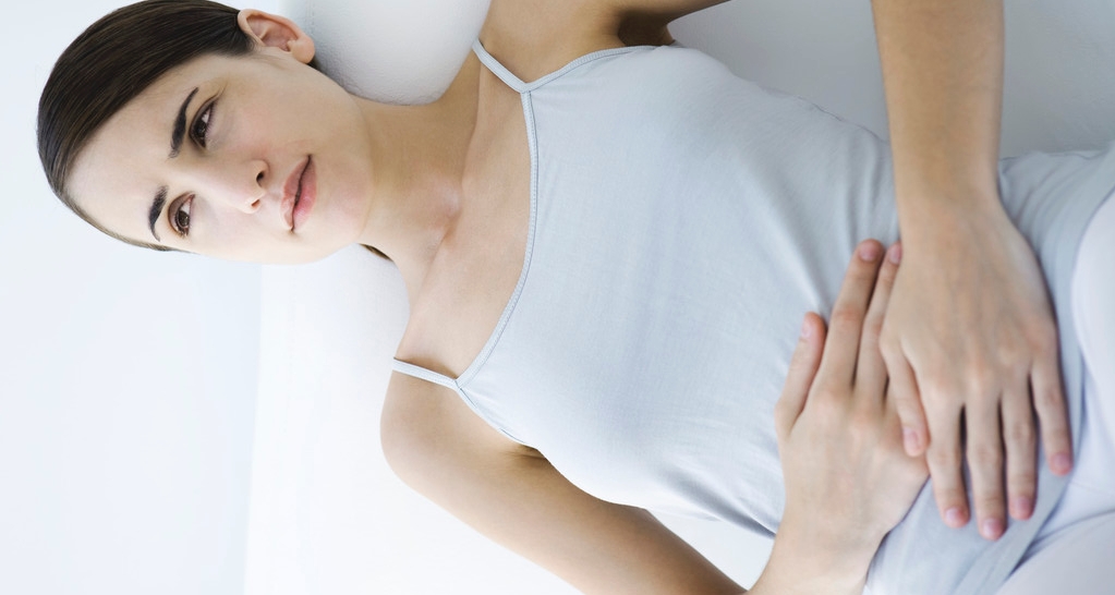 Woman Reclining, Holding Stomach --- Image by © Alix Minde/PhotoAlto/Corbis