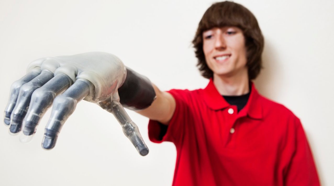 Young man looking at his prosthetic hand over gray background --- Image by © Barry Austin/Moodboard/Corbis