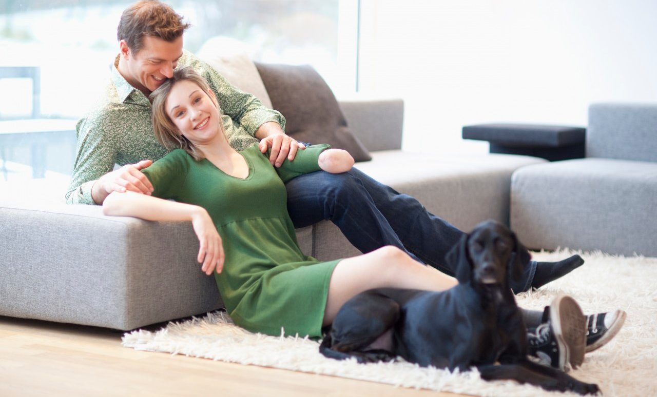 Young couple sitting in living room with dog, woman with amputee arm --- Image by © Altrendo/Juice Images/Corbis