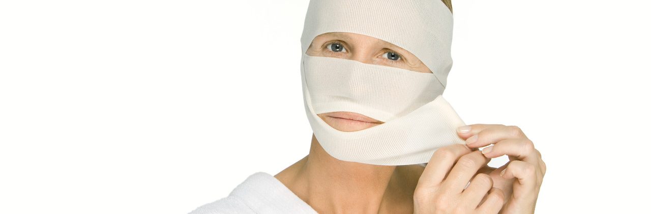 Woman Removing Bandages from Face, Looking at Camera --- Image by © Alix Minde/PhotoAlto/Corbis