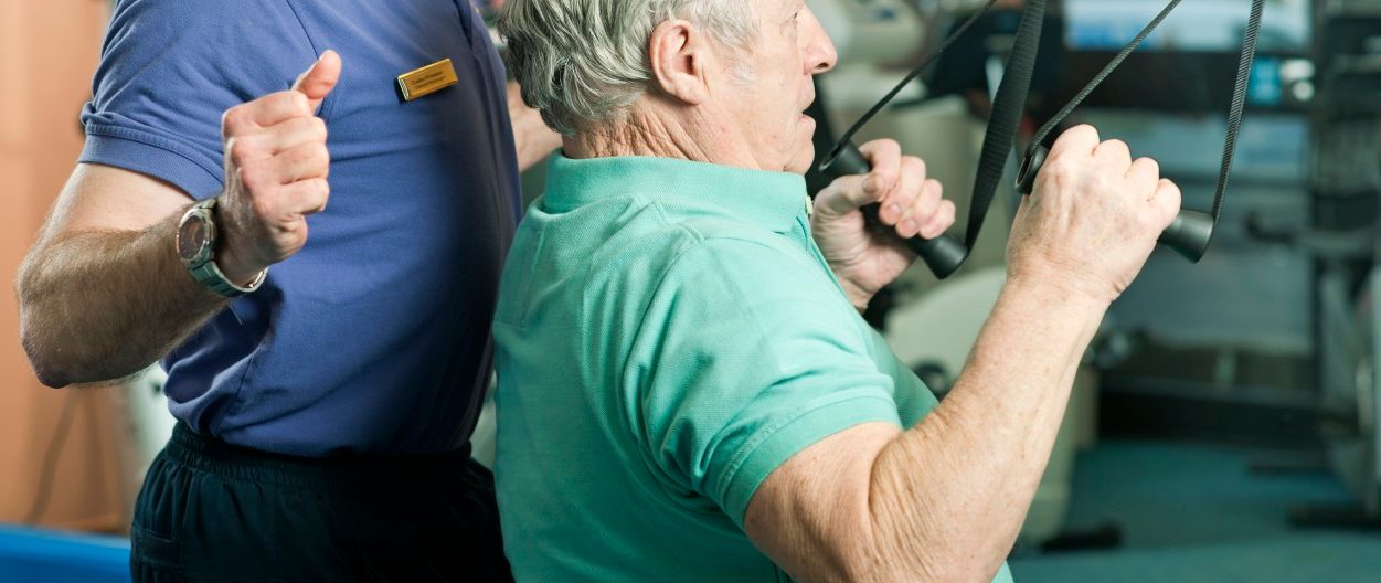 Trainer helping older man exercise --- Image by © Colin Hawkins/cultura/Corbis