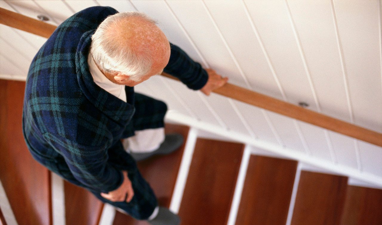 An elderly man carefully descends a staircase --- Image by © Whisson/Jordan/Corbis