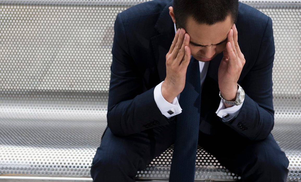 Mixed race businessman sitting on bench with head in hands --- Image by © Dave and Les Jacobs/Blend Images/Corbis