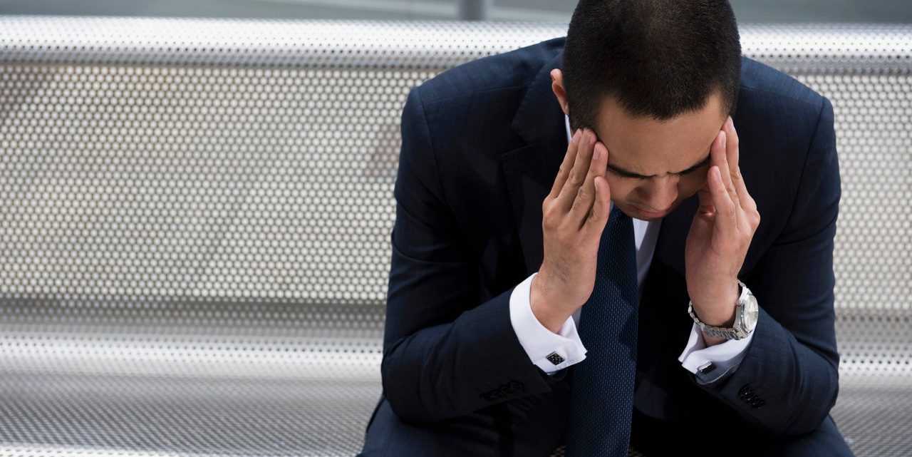 Mixed race businessman sitting on bench with head in hands --- Image by © Dave and Les Jacobs/Blend Images/Corbis