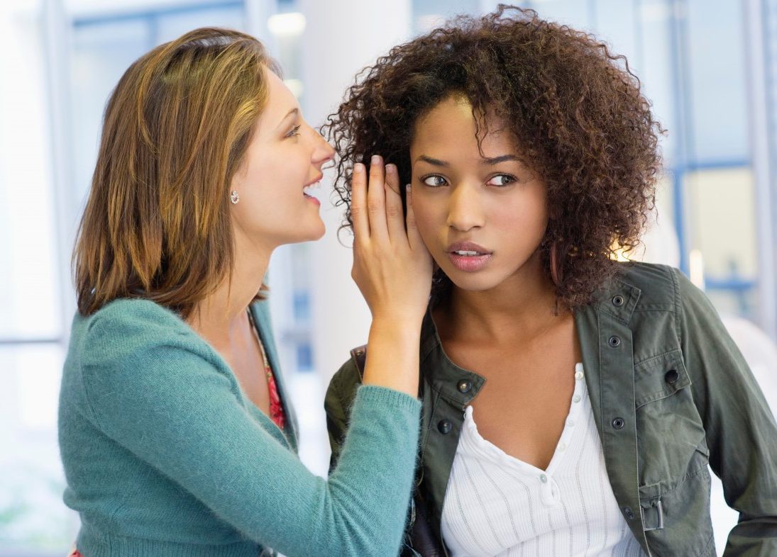 Side profile of a woman whispering in her friend's ear in university --- Image by © Eric Audras/Onoky/Corbis