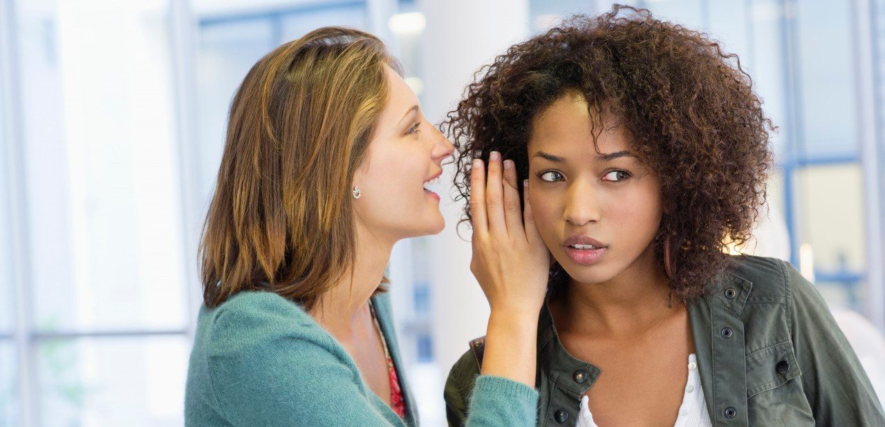 Side profile of a woman whispering in her friend's ear in university --- Image by © Eric Audras/Onoky/Corbis