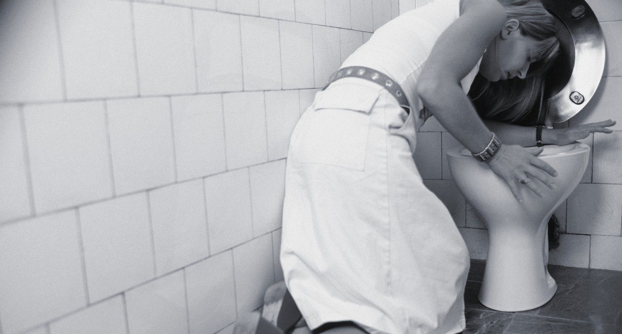 Woman vomiting into toilet --- Image by © Corbis