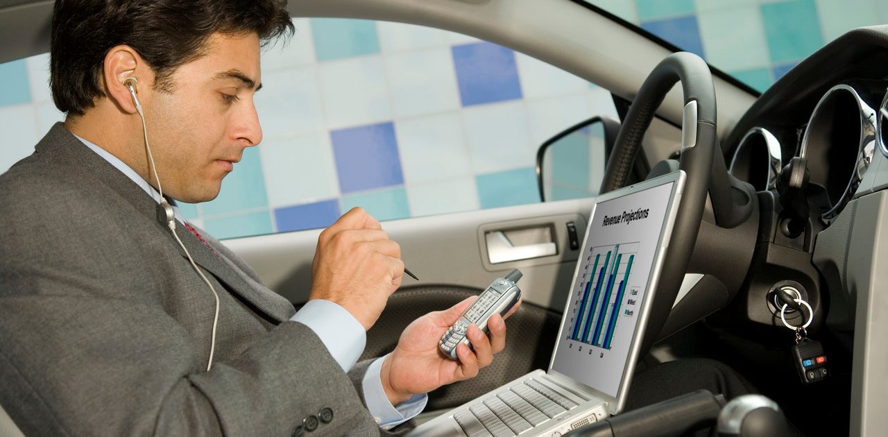 Businessman using his laptop computer and PDA in his car --- Image by © Steve Hix/Somos Images/Corbis