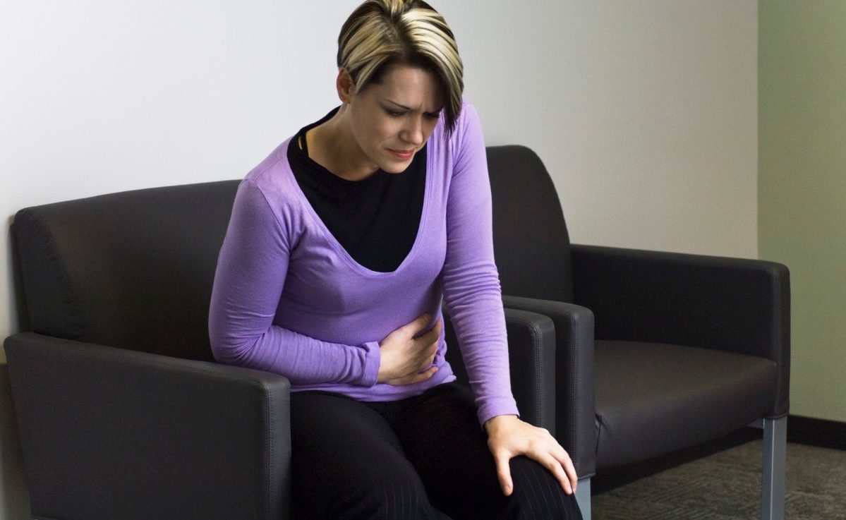 Woman sitting in hospital waiting room holding stomach --- Image by © Michele Constantini/PhotoAlto/Corbis