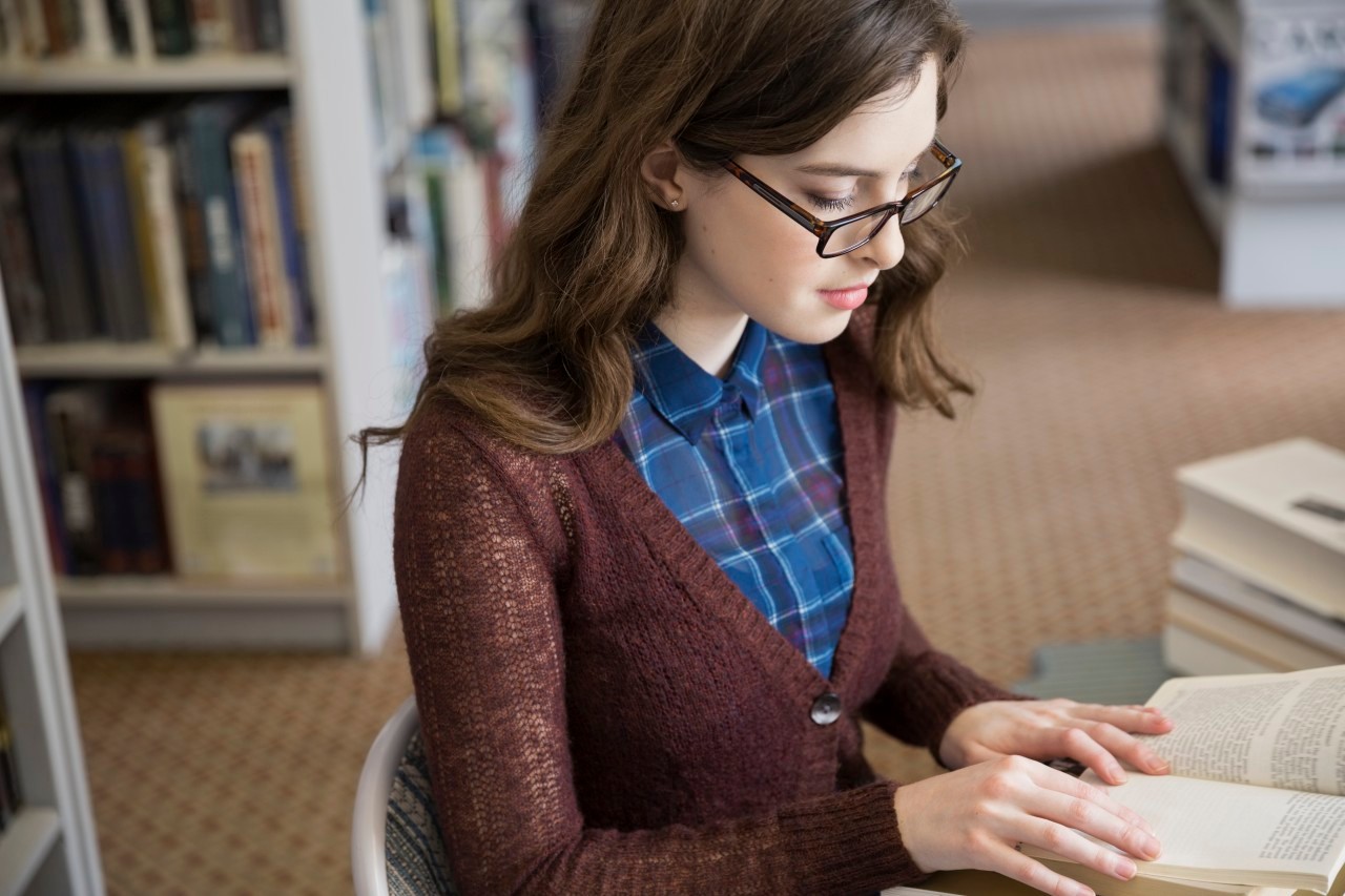 03 Mar 2014 --- Girl in eyeglasses reading book in bookstore --- Image by © Hero Images/Corbis