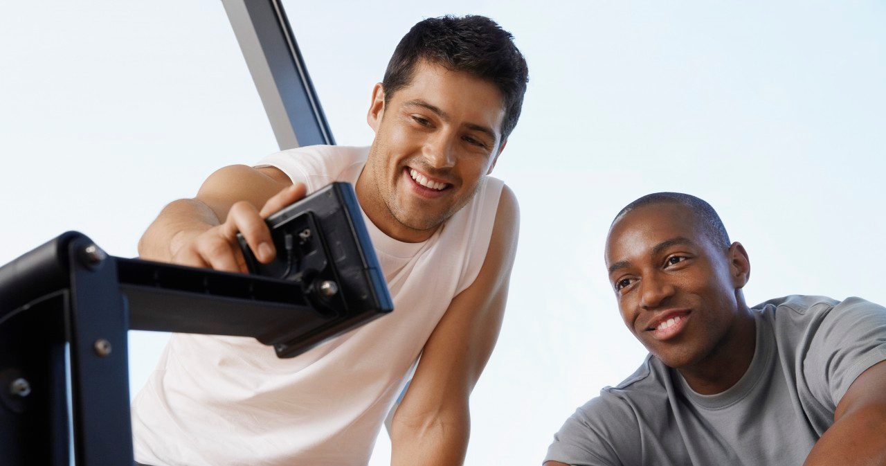 Man showing another man how to use control panel of exercise machine --- Image by © Mike Watson/moodboard/Corbis