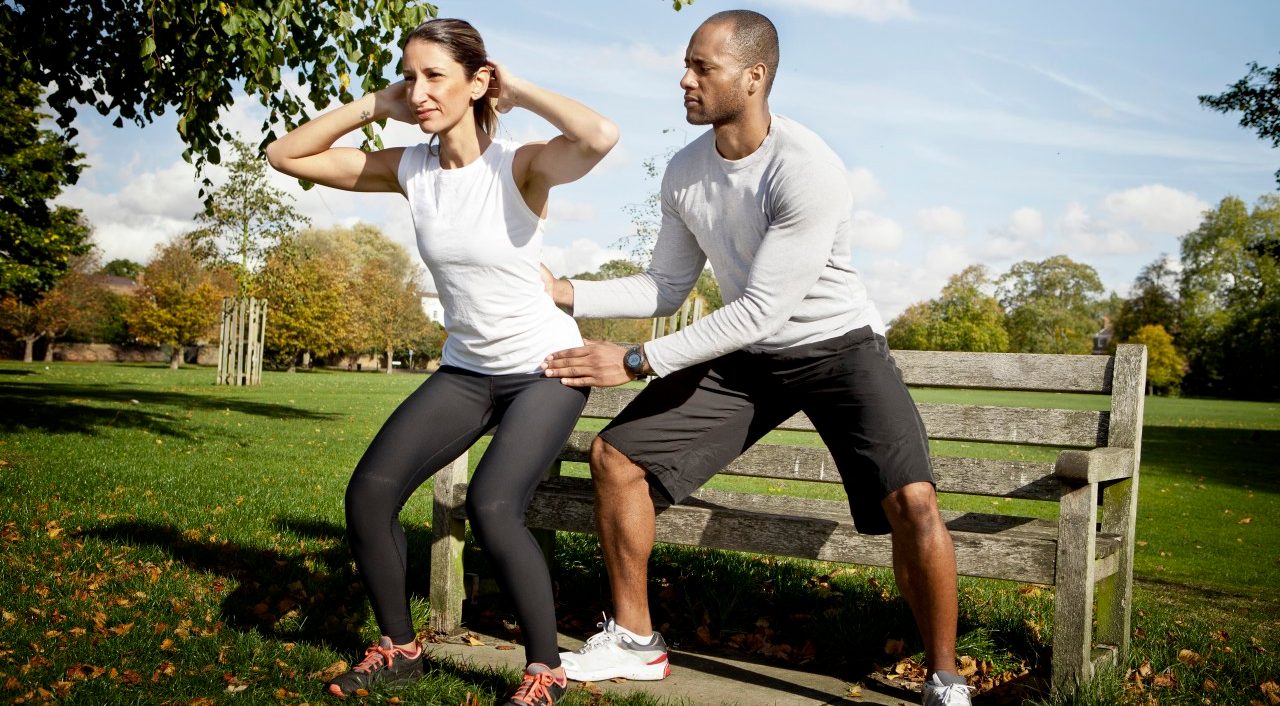 24 Oct 2013 --- Man guiding woman doing squats in park --- Image by © Vincent Starr Photography/Corbis