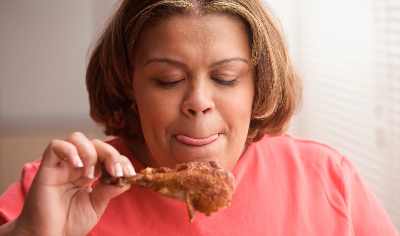 Middle-aged overweight Hispanic woman licking her lips and looking at a piece of fried chicken --- Image by © Jose Luis Pelaez, Inc./Blend Images/Corbis