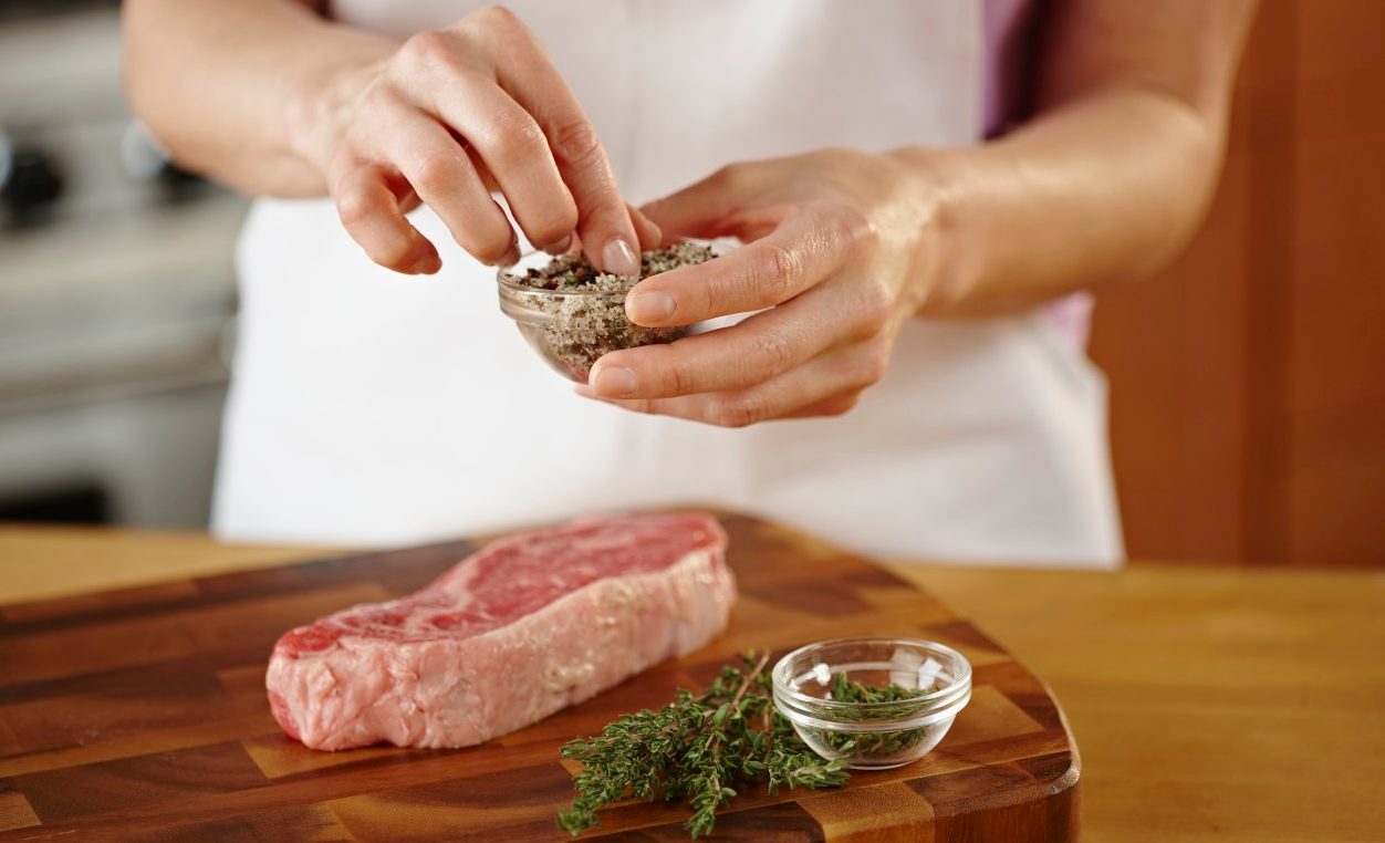 Woman seasoning raw steak with frresh herbs --- Image by © Lew Robertson/Corbis