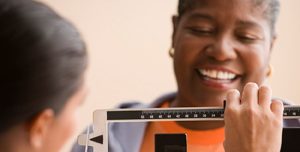 overweight African American woman standing on scale at doctor's office, smiling, happy. 
Source: 85103,PWS_BLP0020114