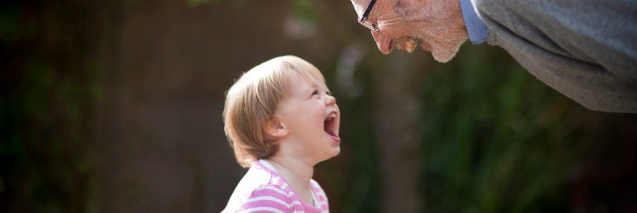 Side profile of Grandfather bending down laughing with his Granddaughter in a garden. --- Image by © MKeal/Corbis