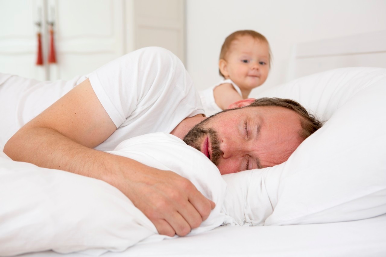 13 Jul 2014 --- Father asleep in bed, baby daughter watching --- Image by © Judith Haeusler/Corbis