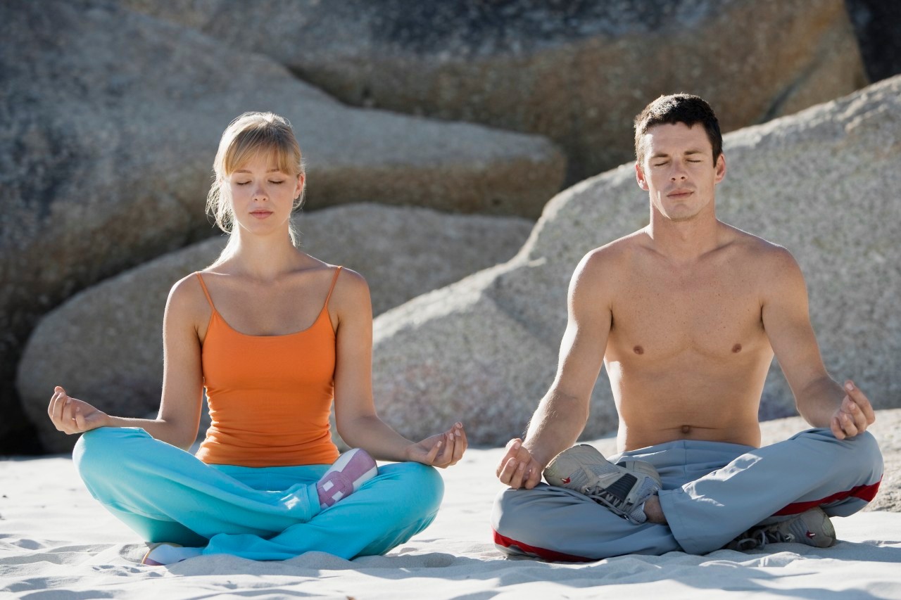 Couple meditating on beach --- Image by © Corbis